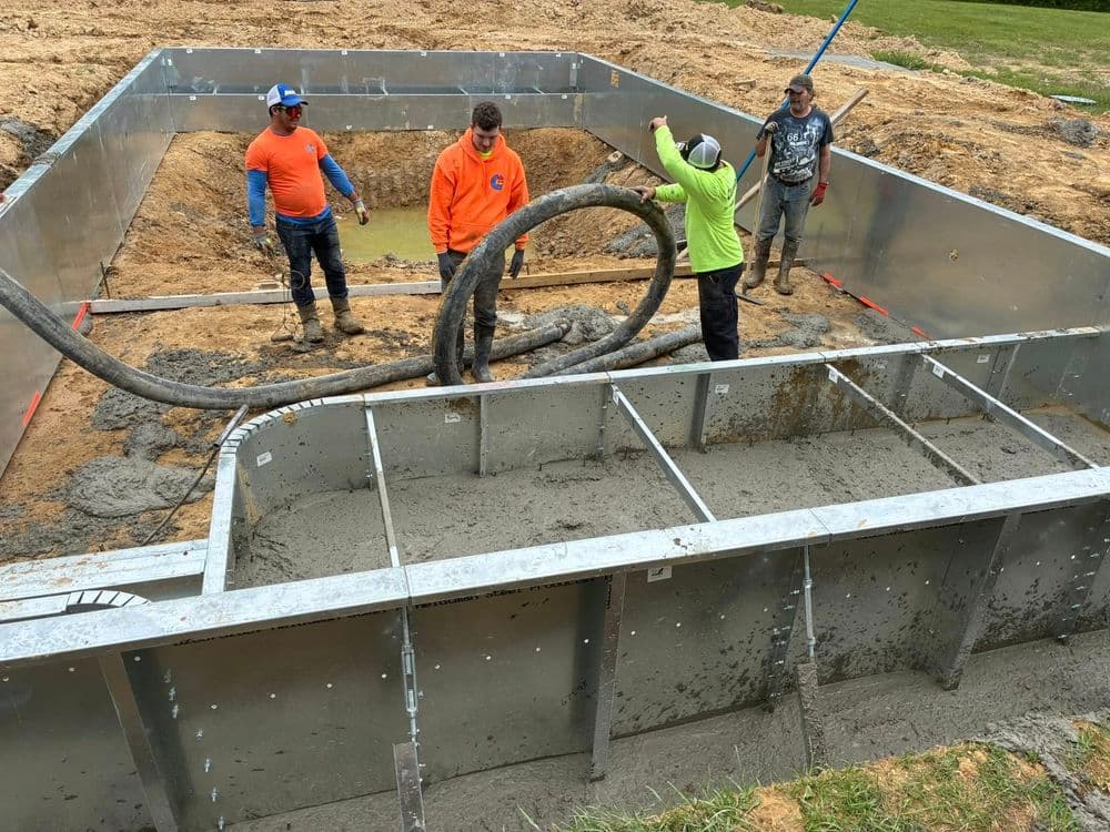 Construction workers pouring concrete into a foundation form at a building site.
